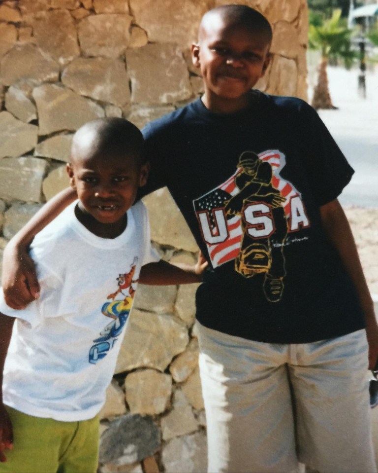 Photo of two young boys standing together in front of a stone wall.