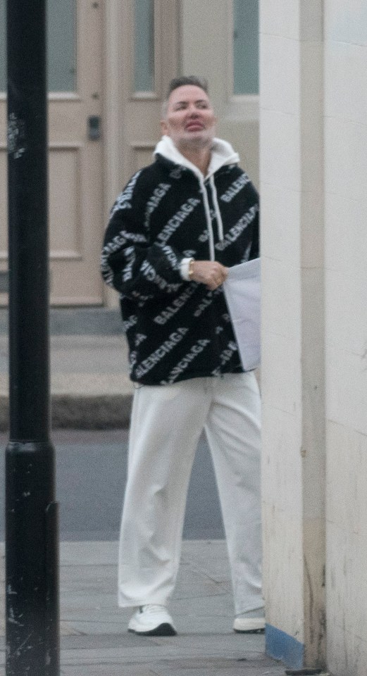 Man in Balenciaga jacket and white pants walking down a street.