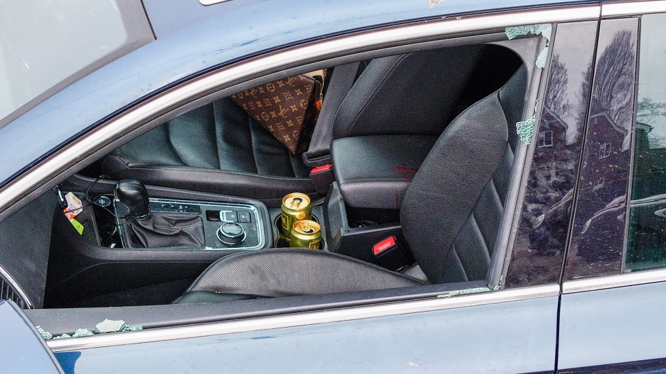 Interior of a car with bullet casings, drinks, and a purse; the car's window is damaged.