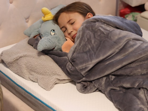 Girl sleeping on a mattress with a stuffed elephant.