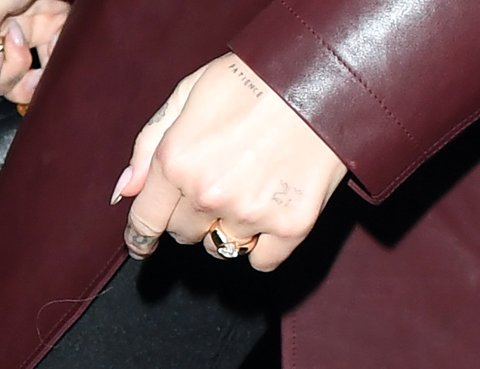 Close-up of Dua Lipa's hand showing a ring and tattoos that read "Patience" and "27".
