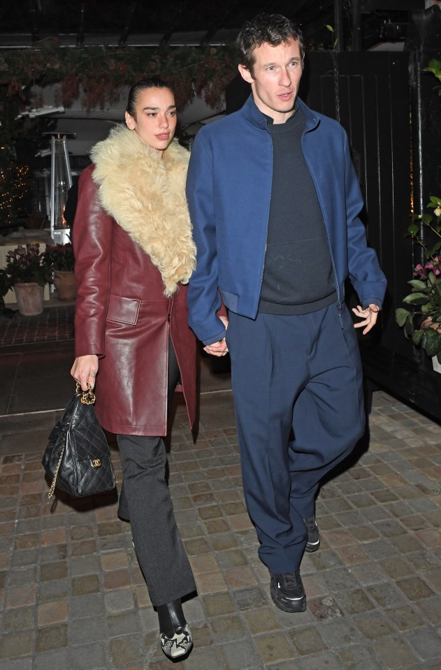 Dua Lipa and Callum Turner holding hands while leaving a restaurant.