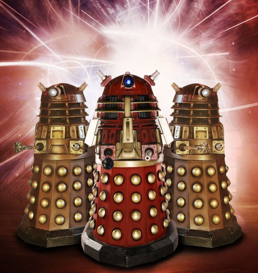 Three Daleks, one red and two bronze, standing together.