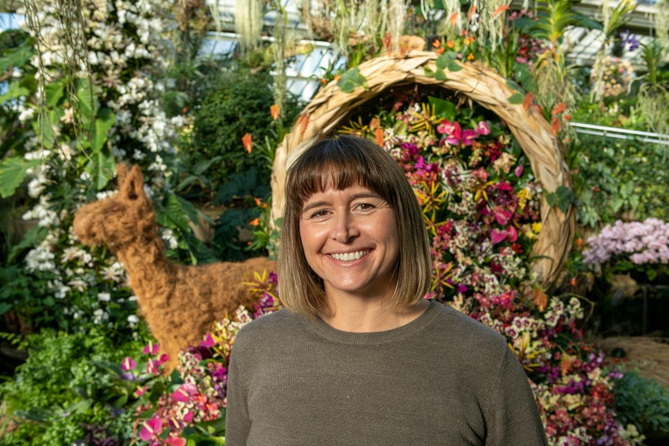 Woman smiling in front of a floral display at Kew Gardens Orchid Festival.