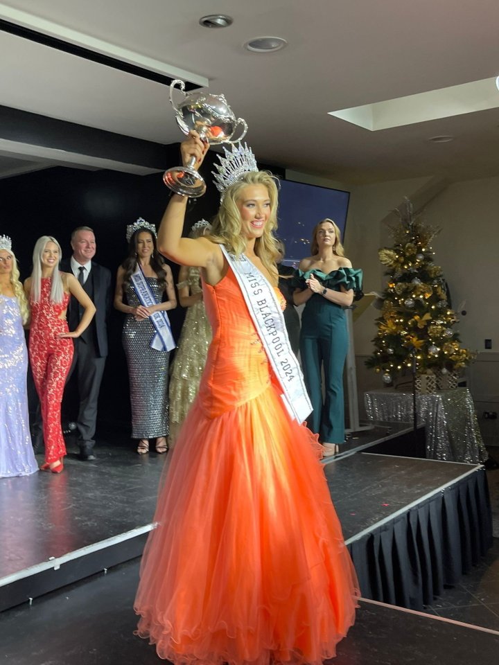 A woman in an orange gown holds a trophy after winning a beauty pageant.
