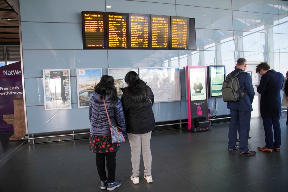 Train schedule board and passengers at a train station.