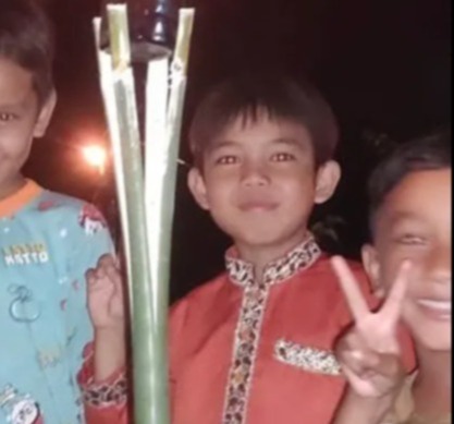 Three boys standing at night near a burning torch.