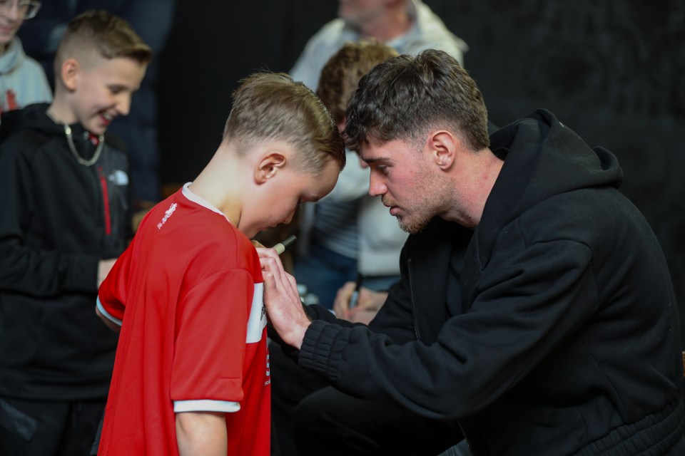 A man signing a young boy's red shirt.