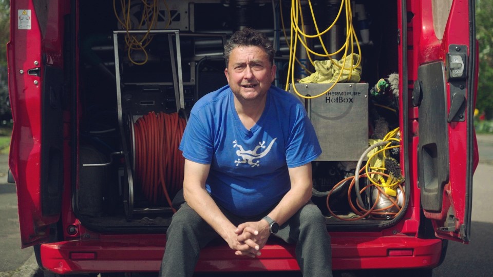 Man sitting in the back of a red van with cleaning equipment.