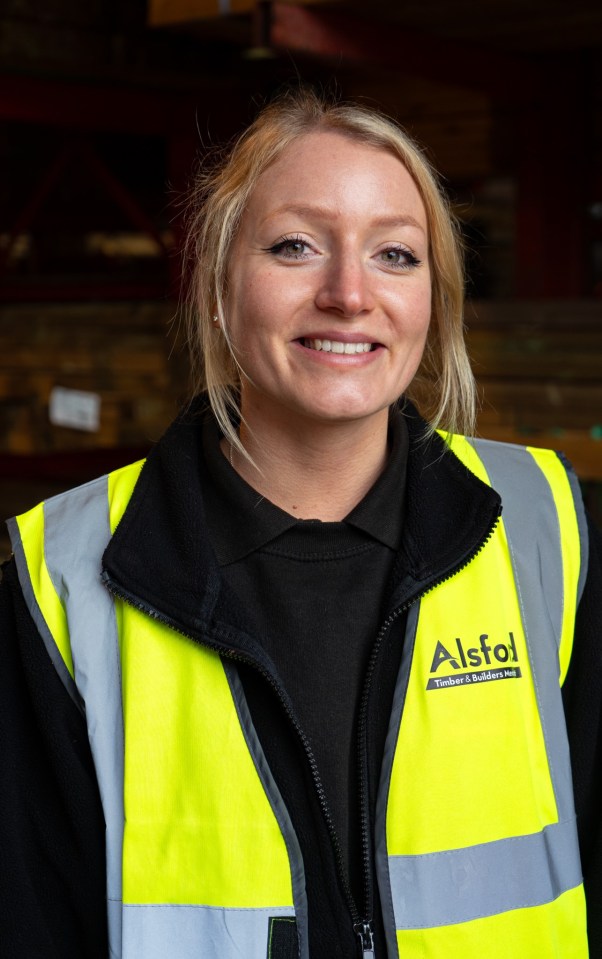 Portrait of a smiling woman wearing a yellow safety vest with the Alsfol Timber & Builders Merchant logo.