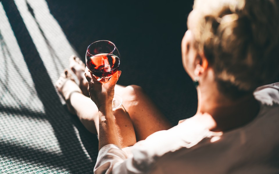 Senior woman enjoying a glass of red wine in sunlight.