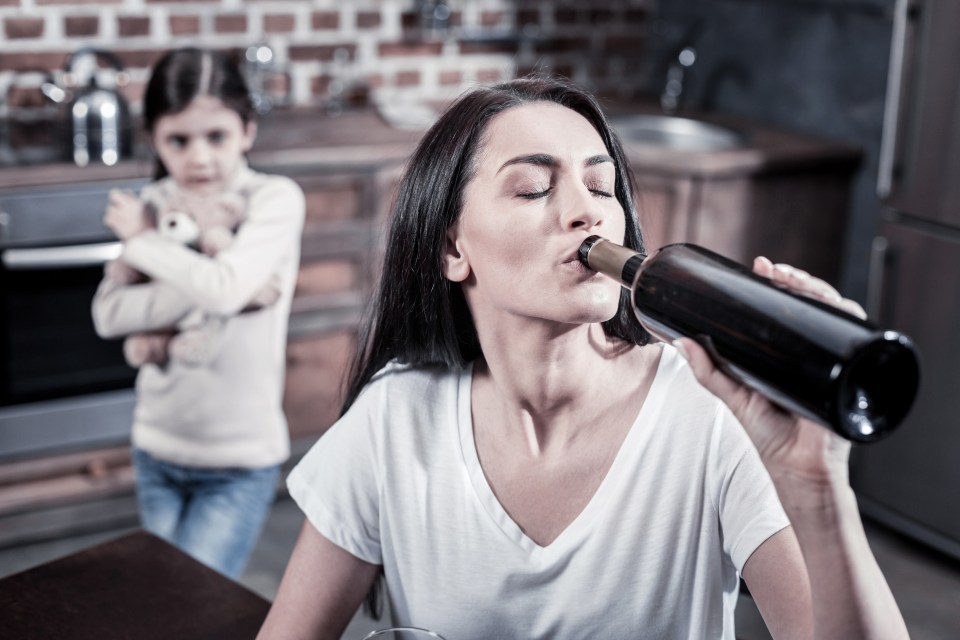 A young woman drinks from a bottle of wine while her young daughter watches sadly.