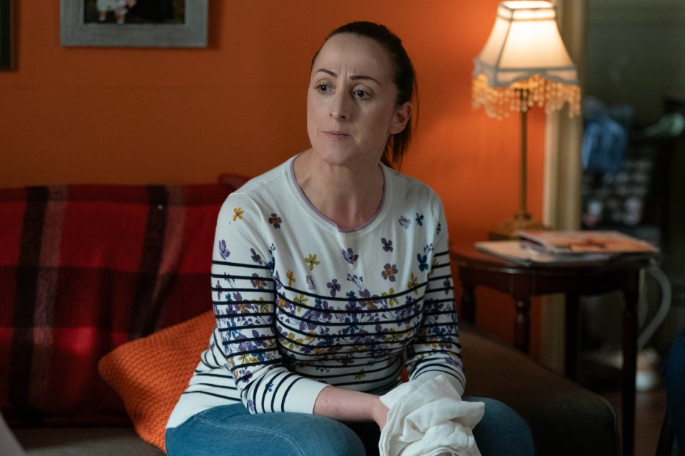 Sonia Fowler from EastEnders sits on a couch.