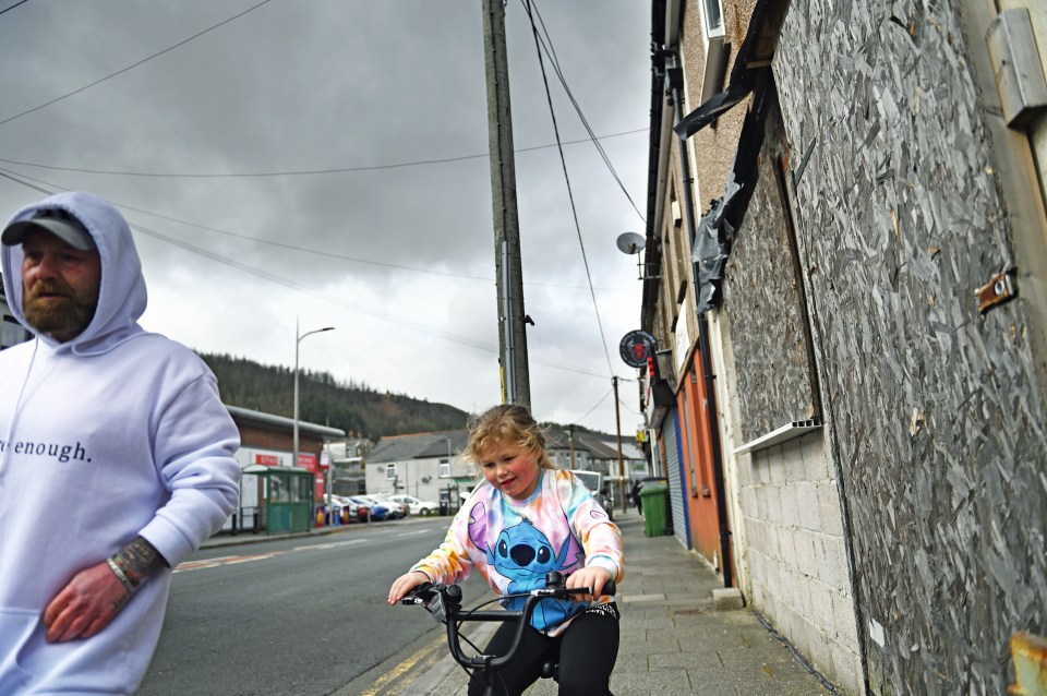 A young girl on a bicycle rides past boarded-up shops in Maerdy, South Wales.