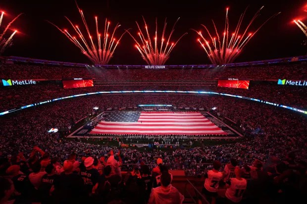 Large American flag displayed on a football field during a fireworks show.