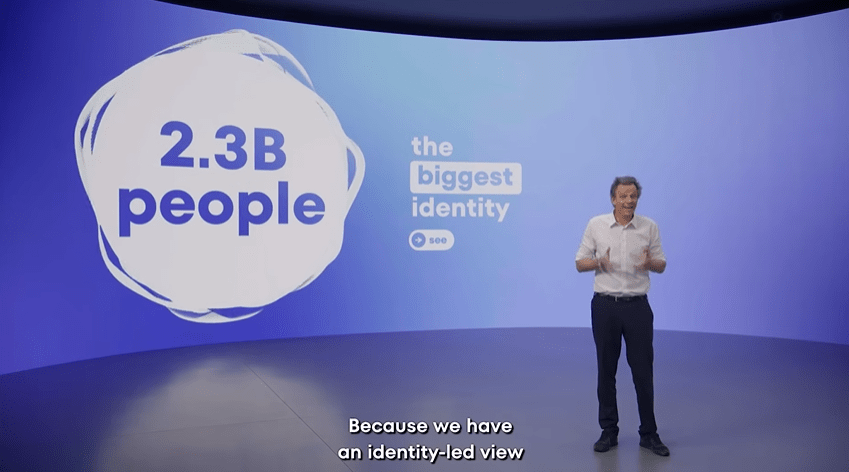 Man presenting in front of a screen showing "2.3B people" and "the biggest identity".