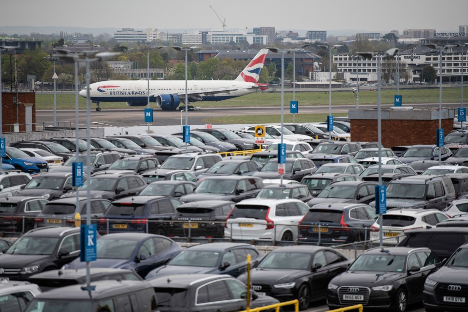 British Airways plane landing at Heathrow Airport behind a large car park.