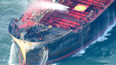 A fire-damaged tanker being hosed down at sea.