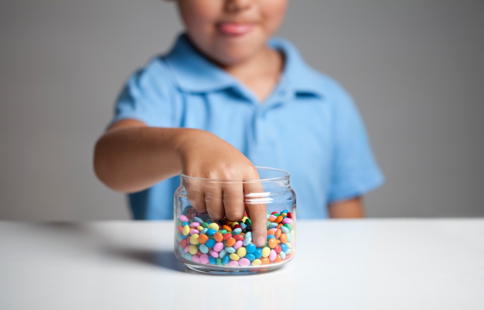 A child's hand reaching into a jar of colorful candies.