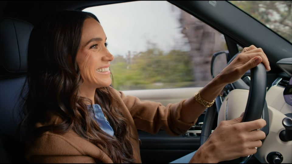 Meghan Markle smiling while driving a car.