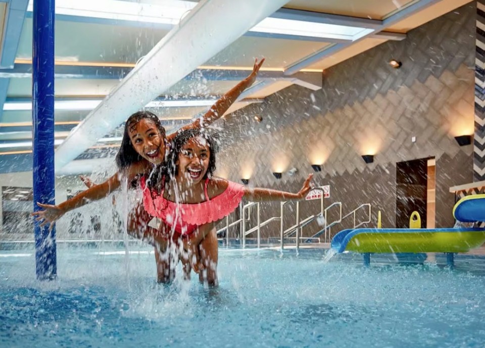 Two girls having fun on a water slide in an indoor pool.