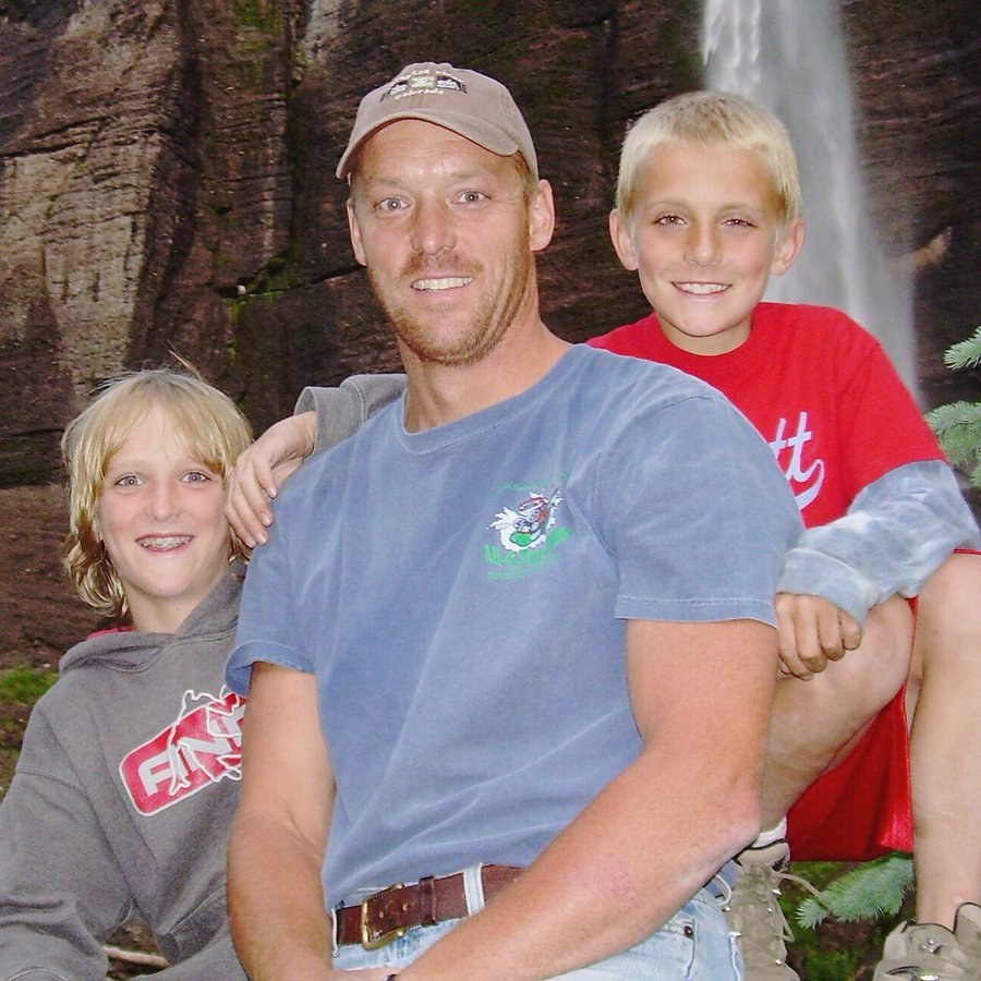 A man and his two sons posing in front of a waterfall.