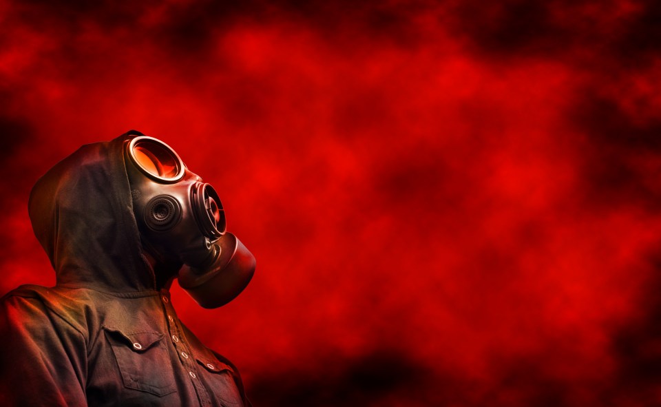 Person in a hooded jacket and gas mask against a red, smoky background.