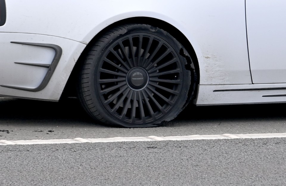 A white luxury car with a flat tire on the side of a motorway.