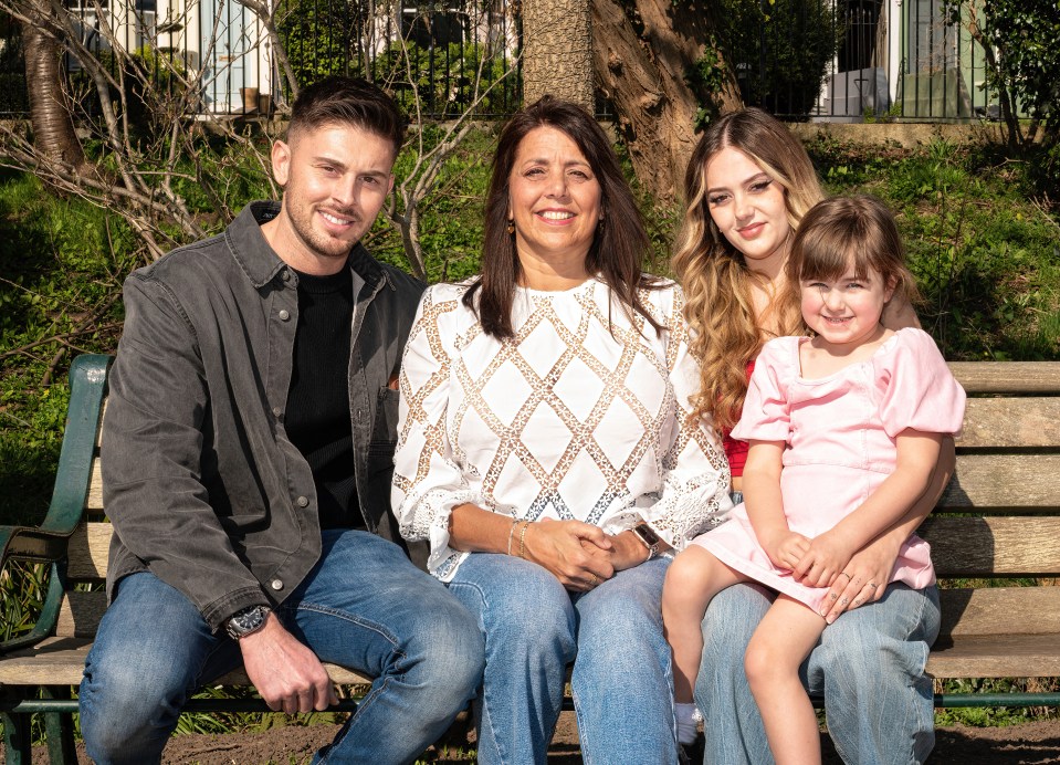 A mother, her adult children, and her grandchild sitting together on a park bench.