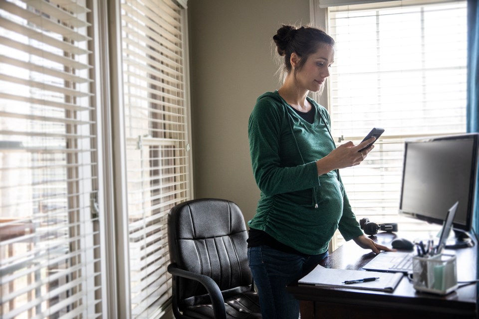 Pregnant woman using a smartphone at her home office desk.