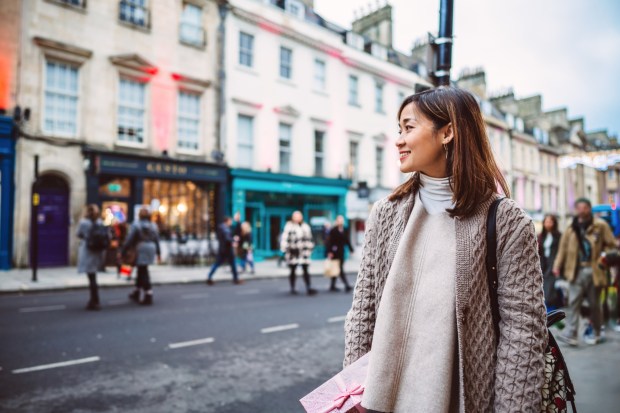 Woman holding a gift box while shopping on a city street.