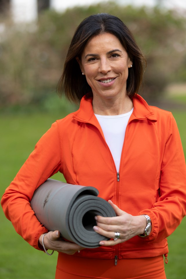 Woman in orange jacket holding a rolled-up yoga mat.