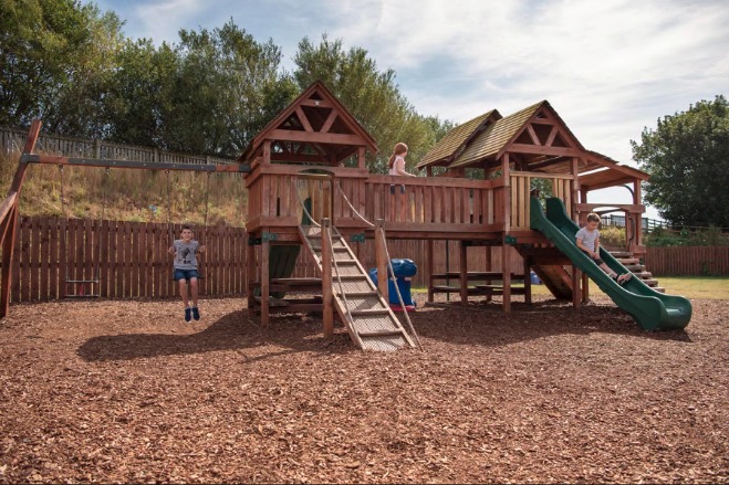 Children playing on a playground with swings and a climbing frame.