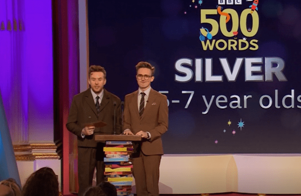 Two men presenting an award at the BBC 500 Words Silver award ceremony for 5-7 year olds.