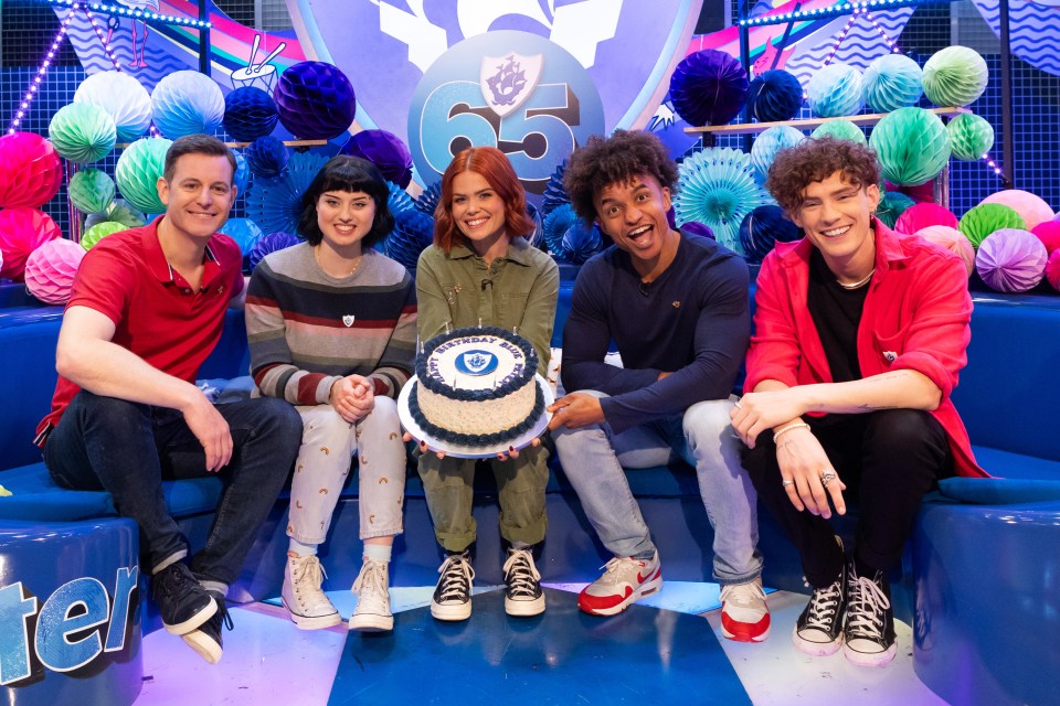 Five presenters on a children's television program celebrate the show's 65th birthday with a cake.