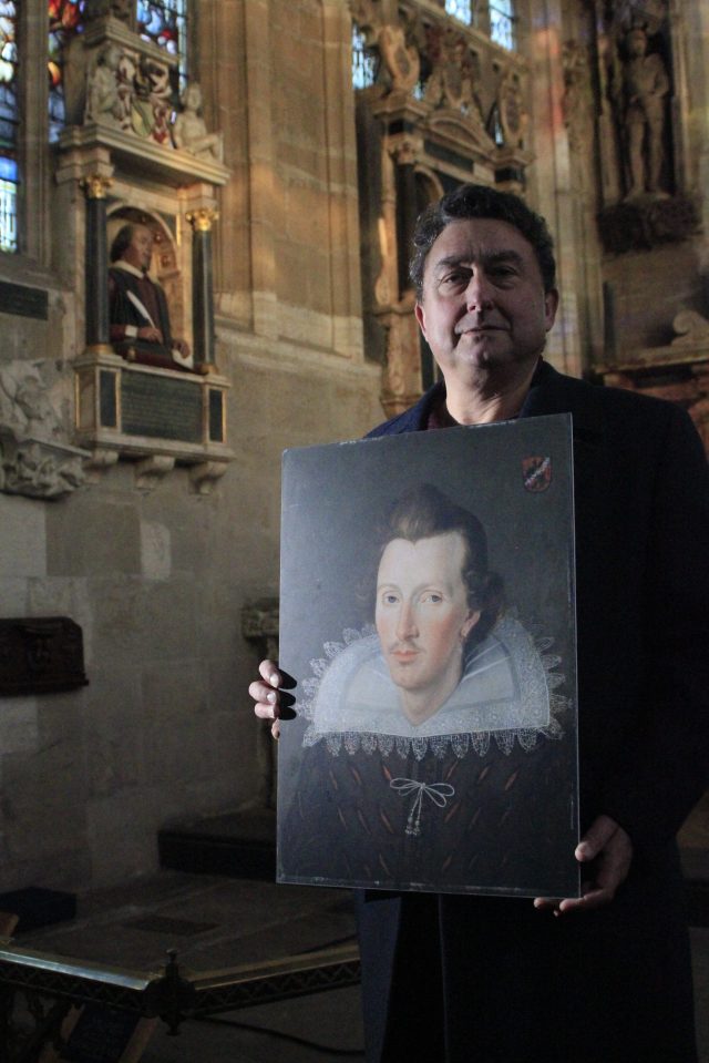 A man in a church holds a portrait of a person wearing a large lace collar.