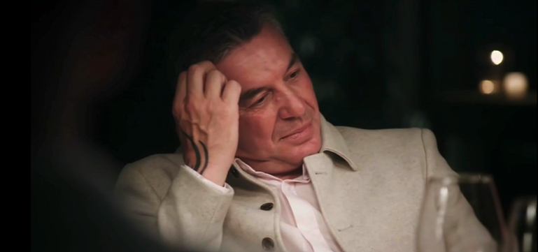 A man sits pensively, hand to his head.