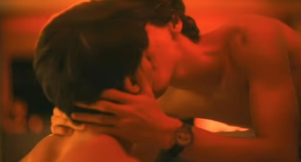 Screenshot of a scene from *The White Lotus* showing two men kissing.