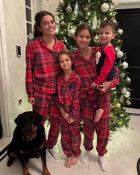 Family in matching red plaid pajamas by a Christmas tree.