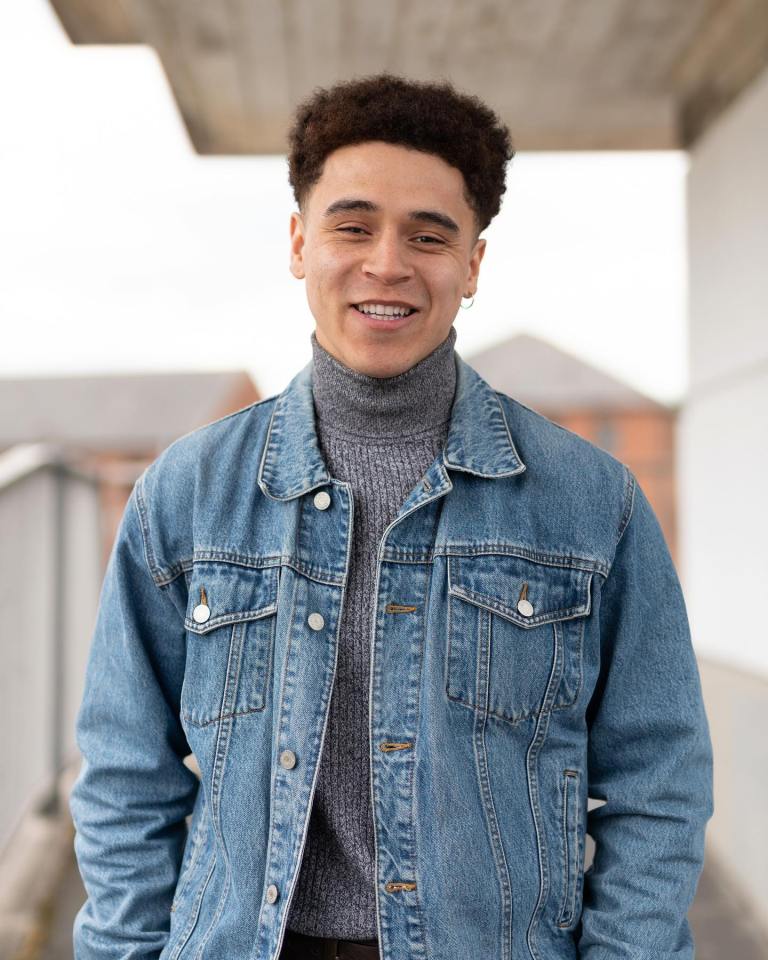 Portrait of a smiling young man wearing a denim jacket and turtleneck.
