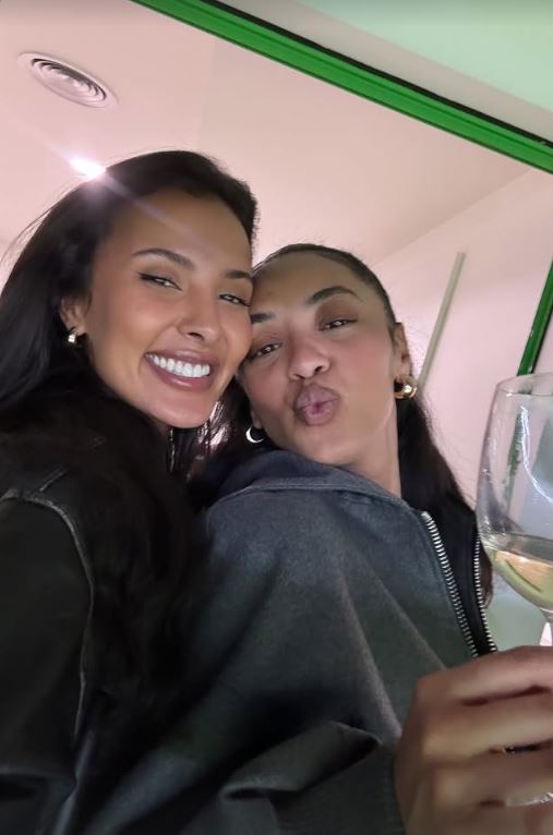 Two women posing together, one holding a glass of wine.