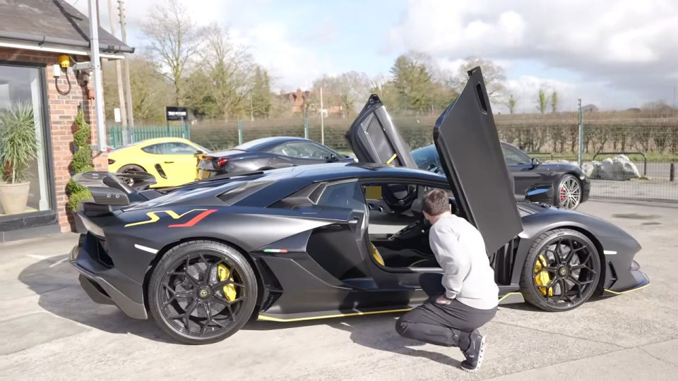 A man crouching beside a black Lamborghini Aventador SVJ with its doors open.