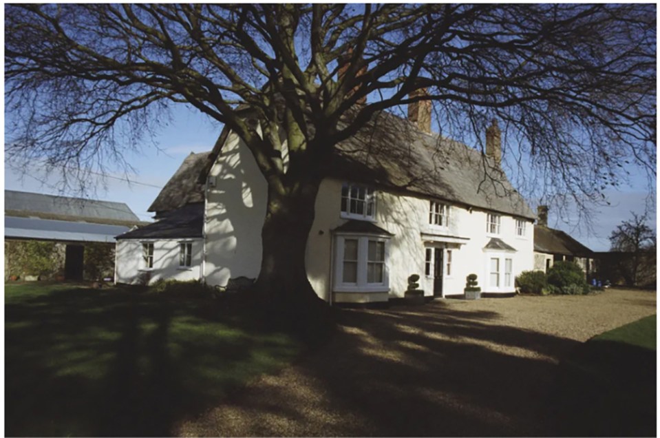Large white farmhouse with a large tree in front.