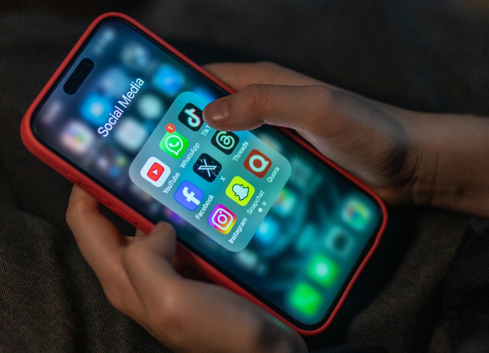 A child's hands holding a smartphone displaying various social media apps.