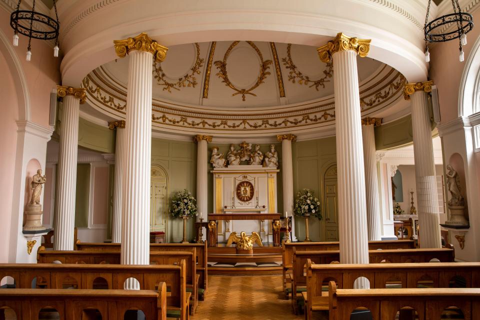 Interior of a chapel with ornate gold detailing and wooden pews.