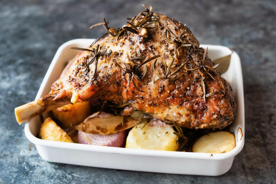 Roast lamb with potatoes and herbs in a white baking dish.