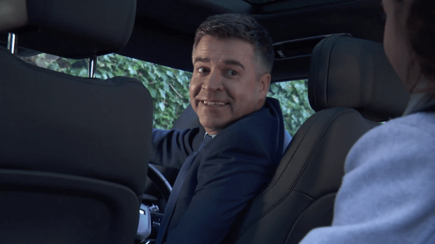 Man in suit smiling in car.