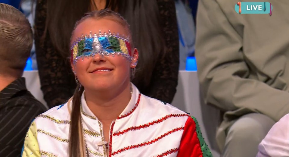 Woman wearing a decorative mask and jacket on a live television show.