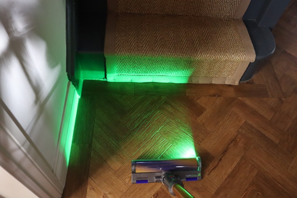 Vacuum cleaner head illuminating a herringbone wood floor with green light.