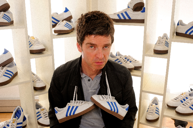 Noel Gallagher holding a pair of Adidas trainers.